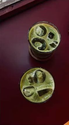 Two iced matcha drinks on a burgundy table.
