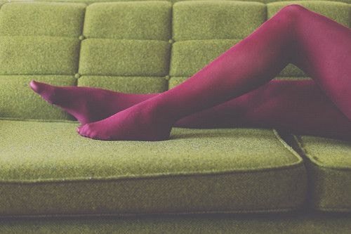 Legs in magenta tights stretched across a green tufted sofa.