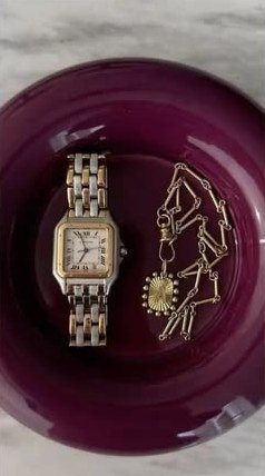 A gold watch and chain necklace in a glossy plum dish.